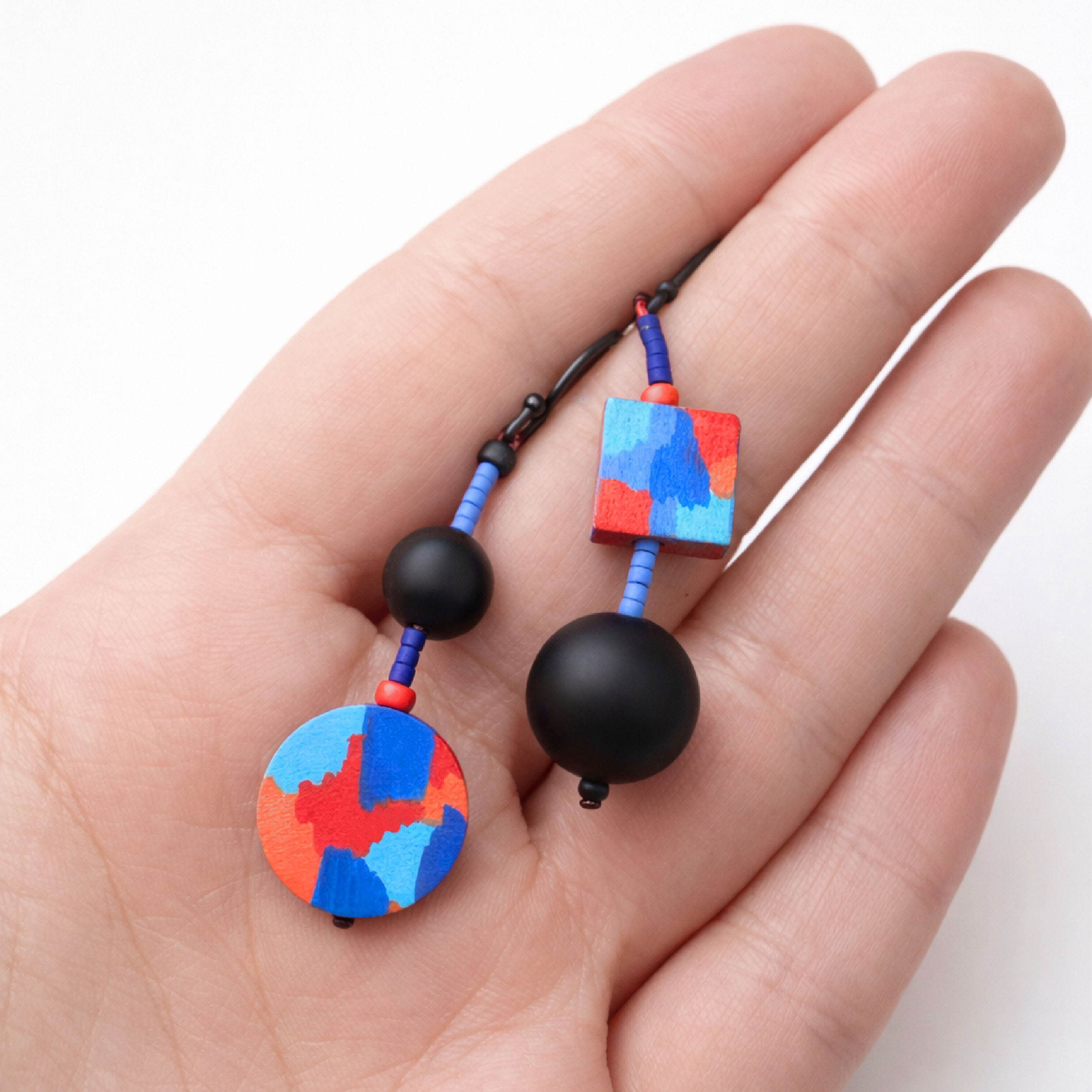 Аsymmetrical earrings held in hand showing texture and colors
